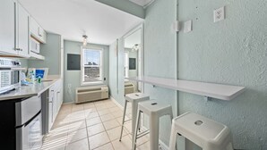 A kitchen with white cabinets, a microwave, and a stove. There are two white stools and a white shelf. - Beachview 312 | Across from beach (Gulf Shores)