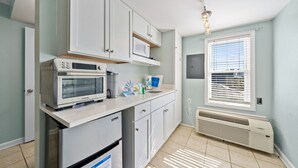A kitchen with white cabinets, a microwave, a refrigerator, and a window with blinds. - Beachview 312 | Across from beach (Gulf Shores)