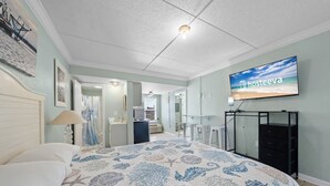 A bedroom with a bed, a TV mounted on the wall, and a desk with chairs. - Beachview 312 | Across from beach (Gulf Shores)