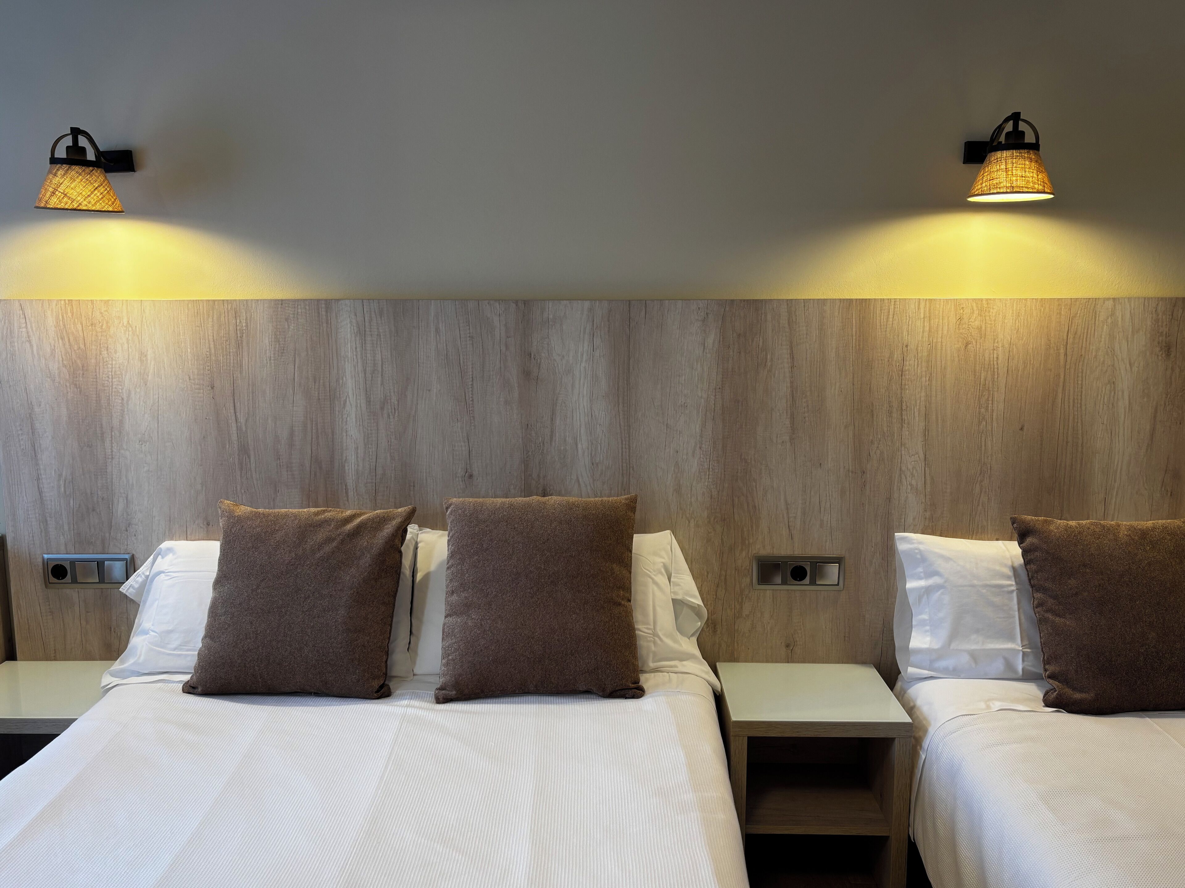 Une chambre d’hôtel avec deux lits, chacun doté d’un oreiller marron et d’un oreiller blanc, ainsi que de deux appliques murales.