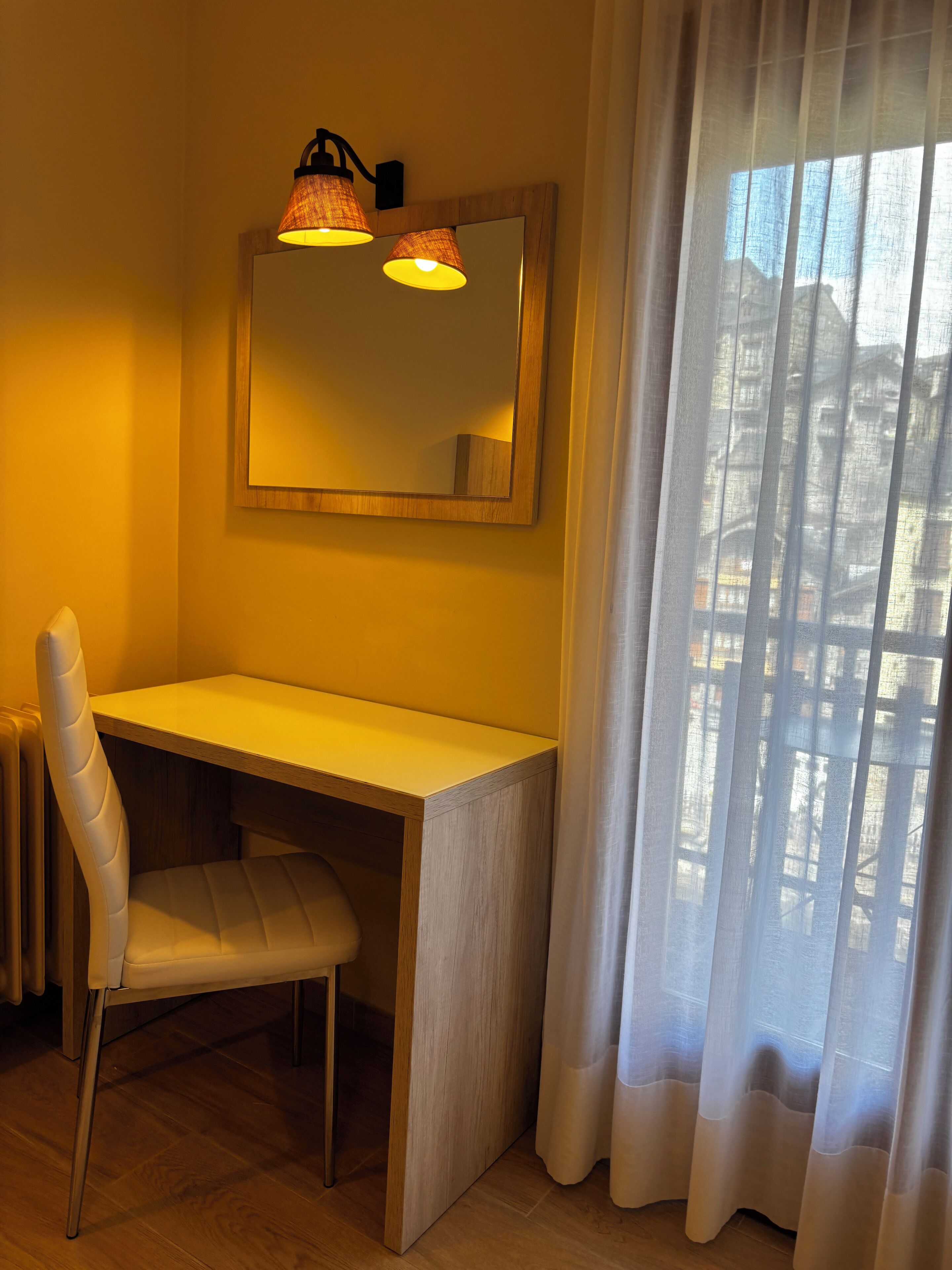 A small, well-lit room with a wooden desk, a chair, and a large mirror above the desk.
