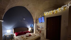 Une chambre avec une arche en pierre, un lit avec des oreillers rouges, un téléviseur fixé au mur et une petite table avec une lampe.