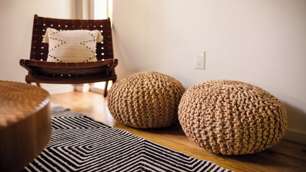 A wooden chair with a white pillow, two knitted poufs, and a black and white rug on a wooden floor. - Villa Sea Breeze (Roatan)
