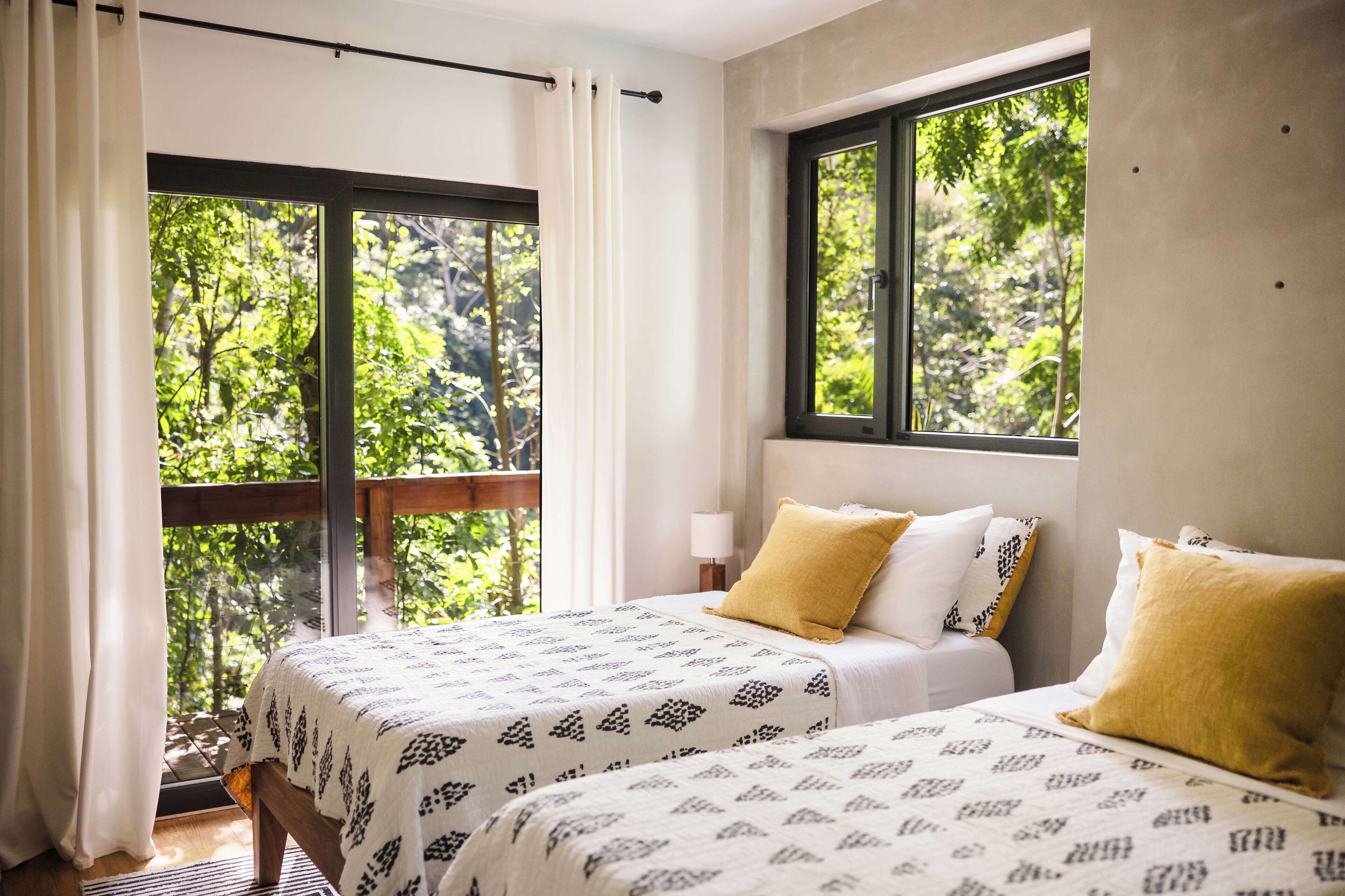 A bedroom with two beds, a window with a view of trees, and a balcony.