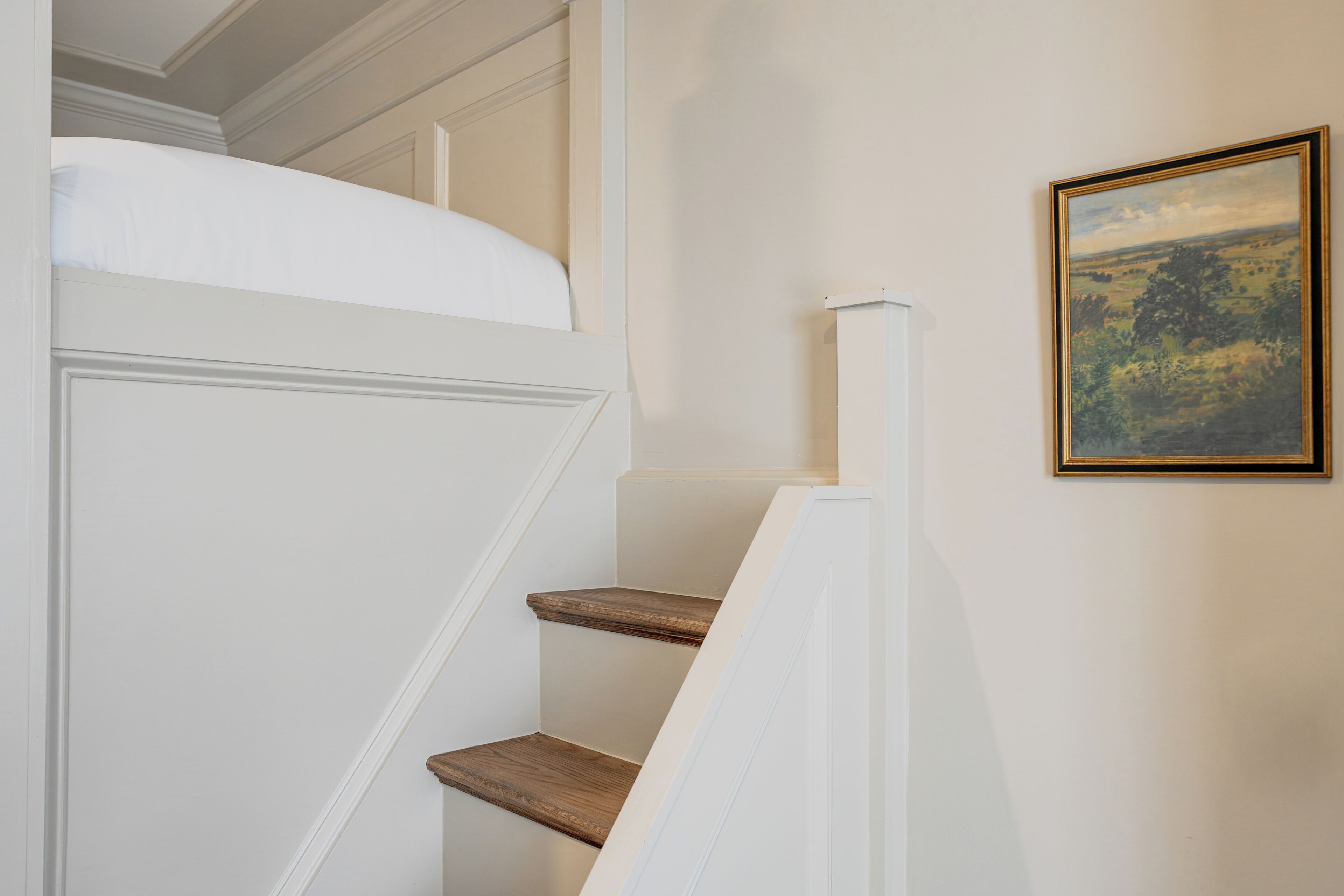 A staircase with a white wall and a framed landscape painting.