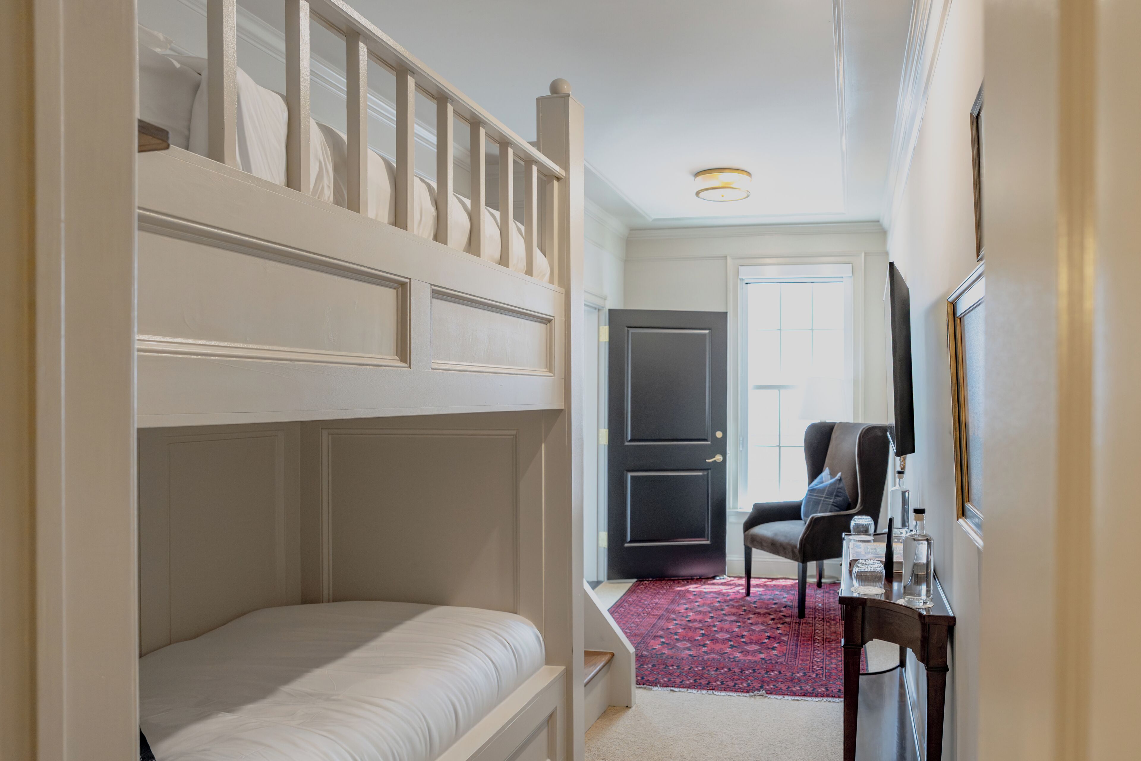 Een kamer met een stapelbed, een bureau met stoel, een televisie en een deur naar een andere kamer.