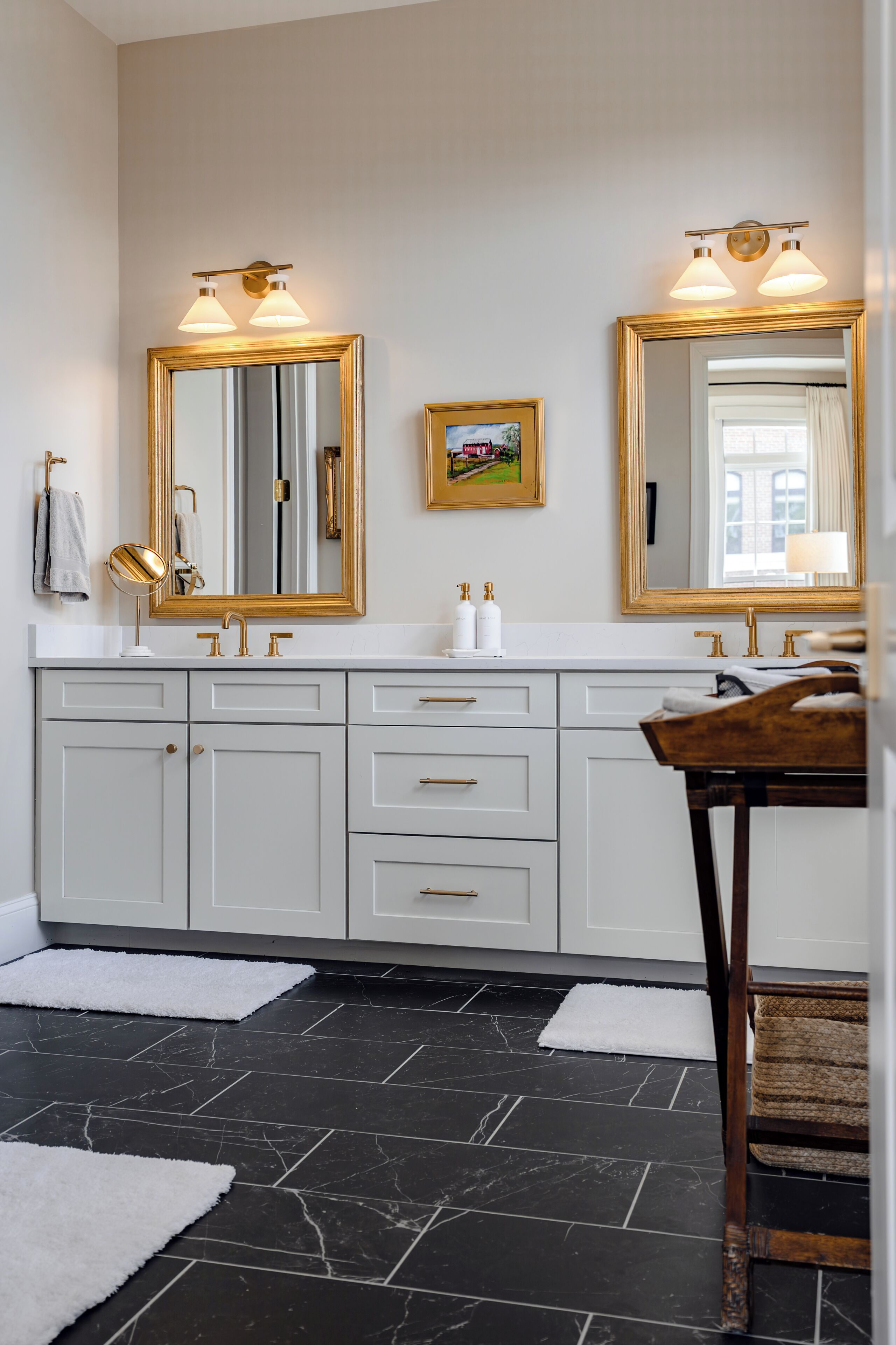 A bathroom with a white vanity, gold fixtures, and a black tiled floor.