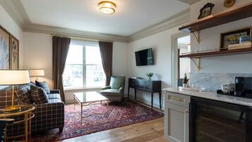Una sala moderna con sofá, sillón, mesa de centro y televisor. Se observa un área de cocina con encimera y mesa de comedor.