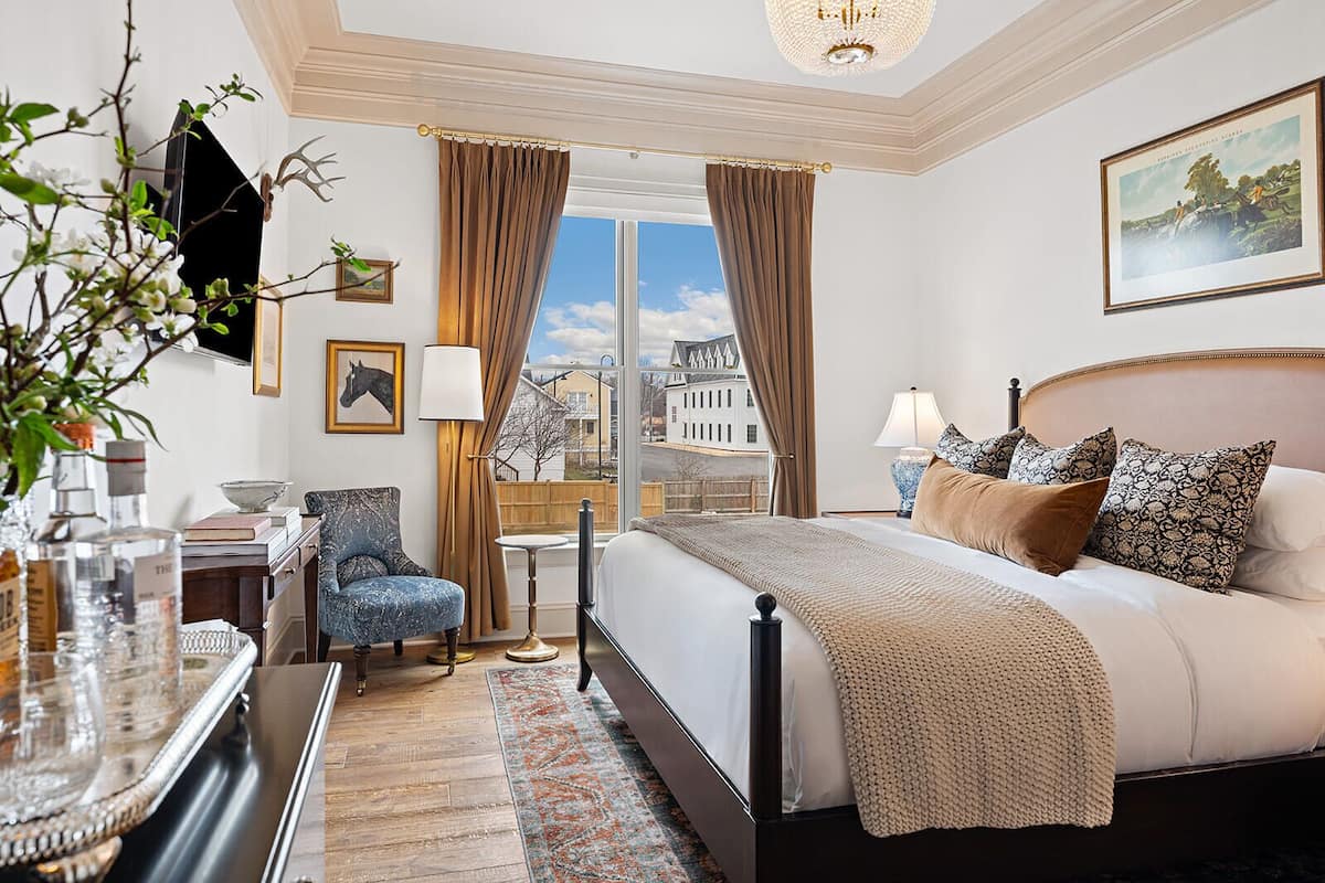 Ett hotellrum med en stor säng, en stol, ett skrivbord och utsikt över stadsbilden genom fönstret.