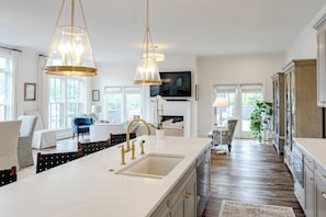 A modern kitchen with a large island, pendant lights, and a flat-screen TV mounted above the island. - Hotel Burg (Leesburg)
