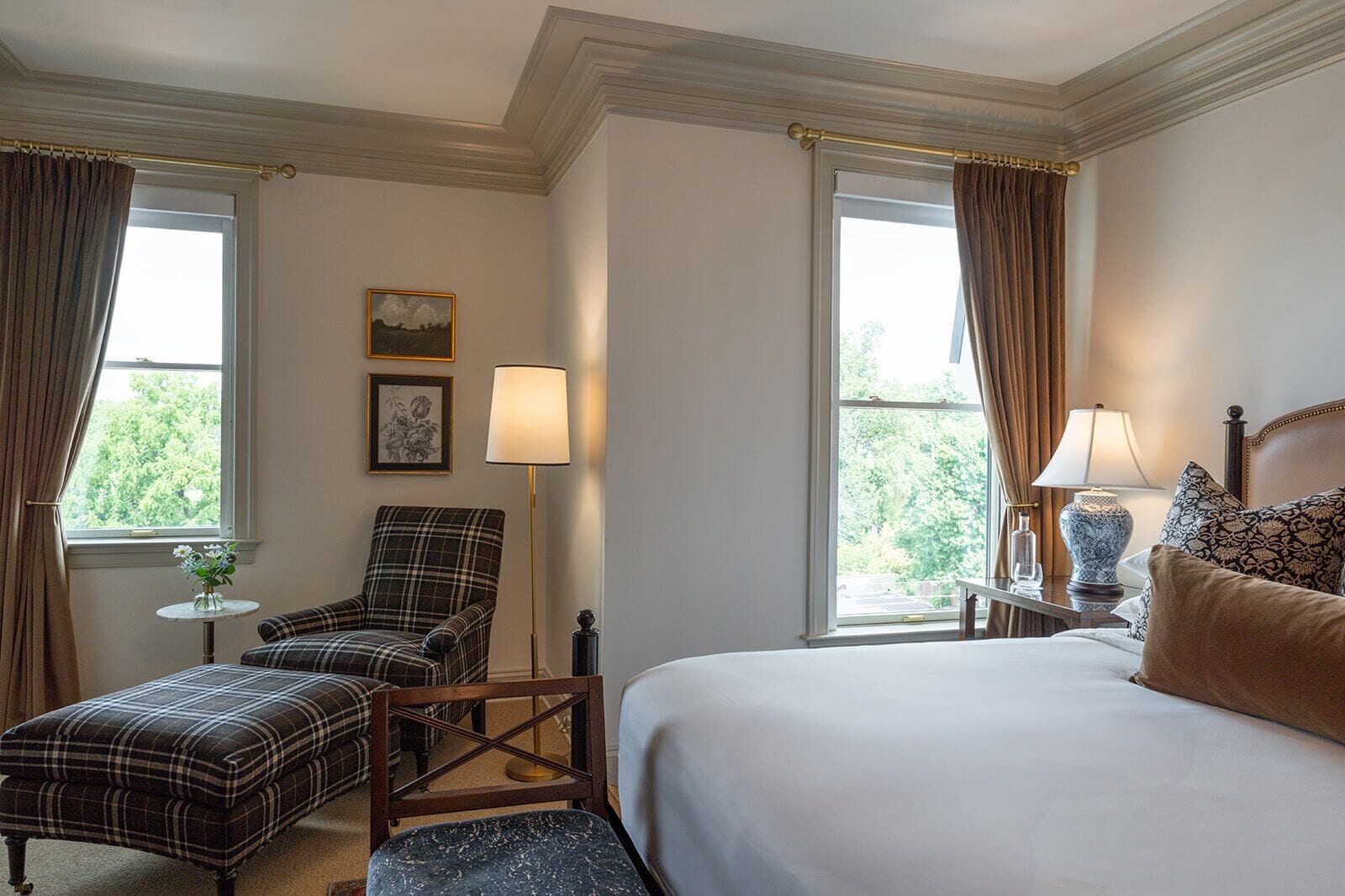 A hotel room with a bed, a chair, two lamps, and a small table with a vase of flowers.