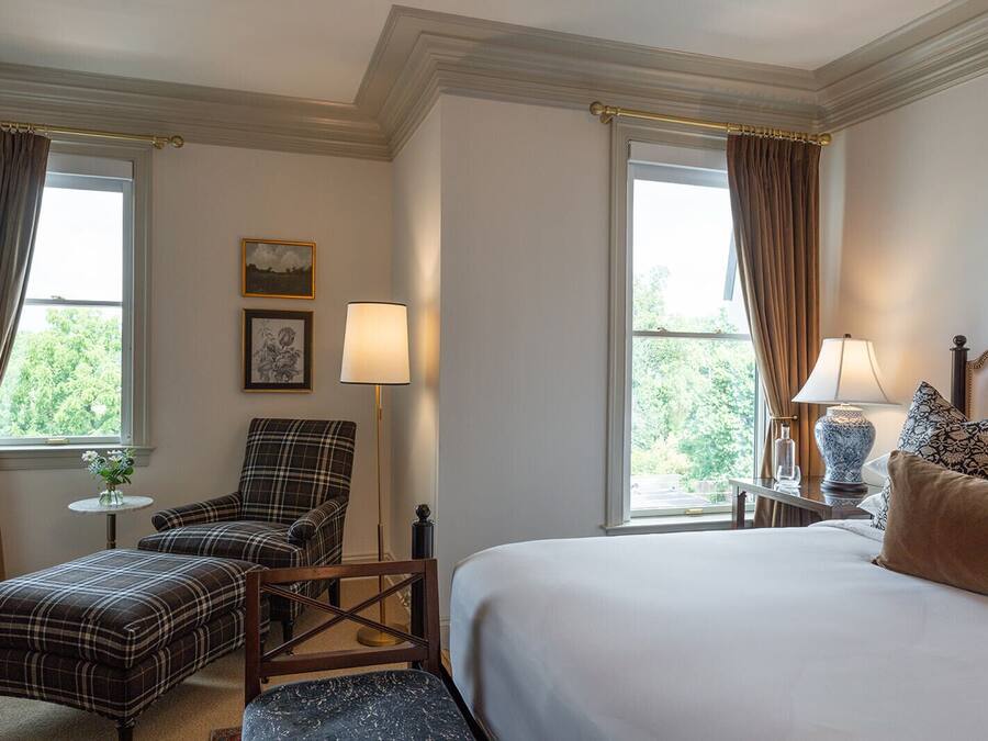 A hotel room with a bed, a chair, two lamps, and a small table with a vase of flowers.