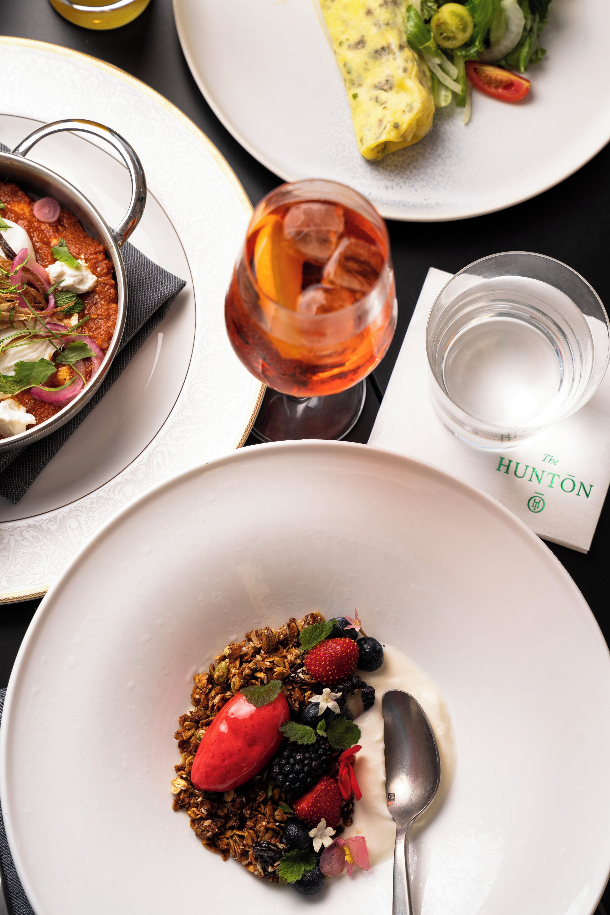 A dining table with plates of food, a glass of drink, and a napkin with "The HUNTON" logo.