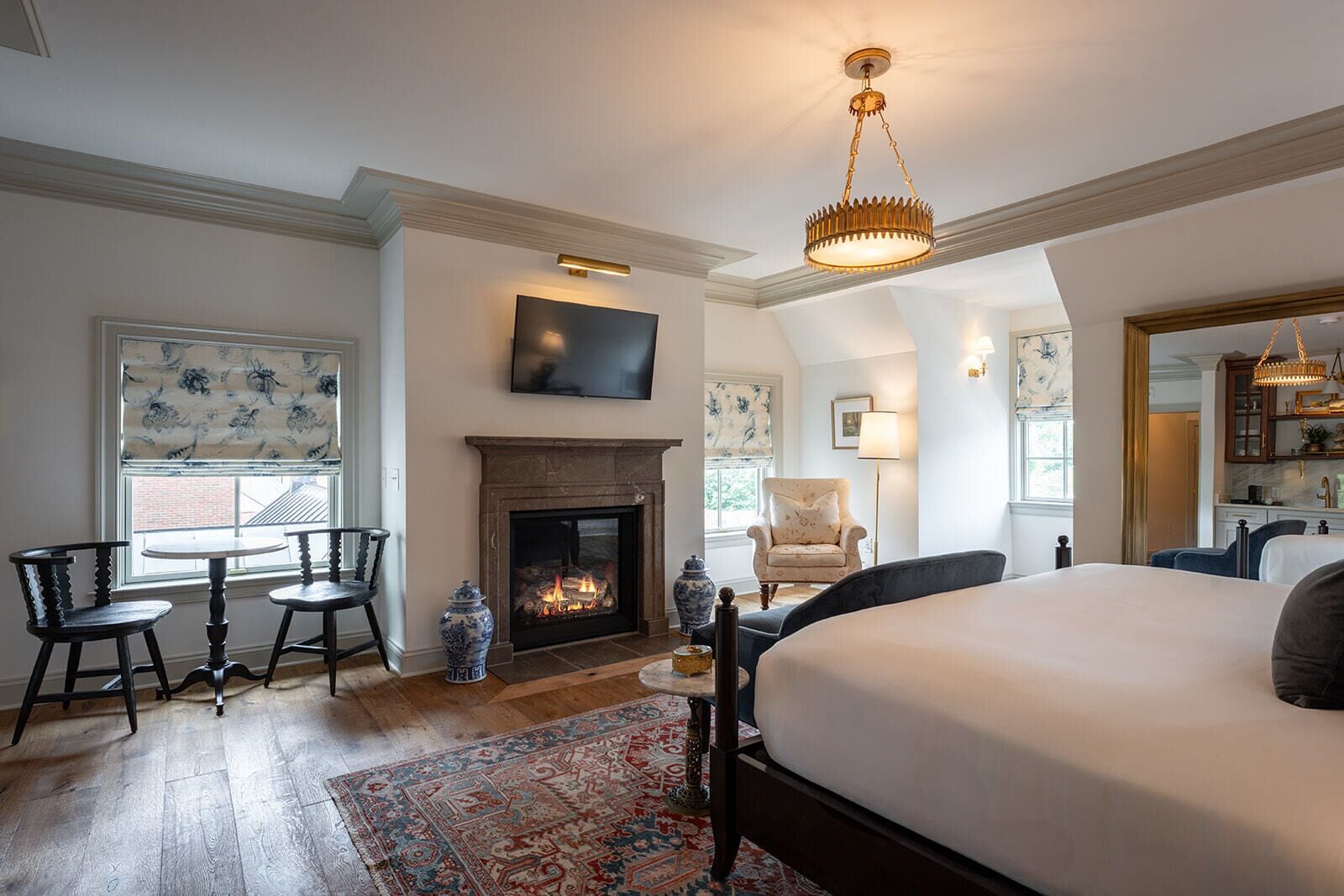 A bedroom with a large bed, a fireplace, a TV, and a dining area with chairs.