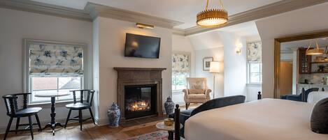 A bedroom with a large bed, a fireplace, a TV, and a dining area with chairs.