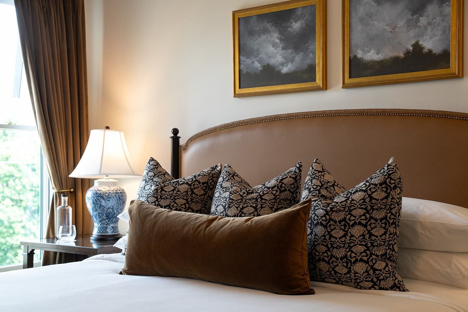 A neatly made bed with patterned pillows, a bedside lamp, and two framed pictures on the wall.