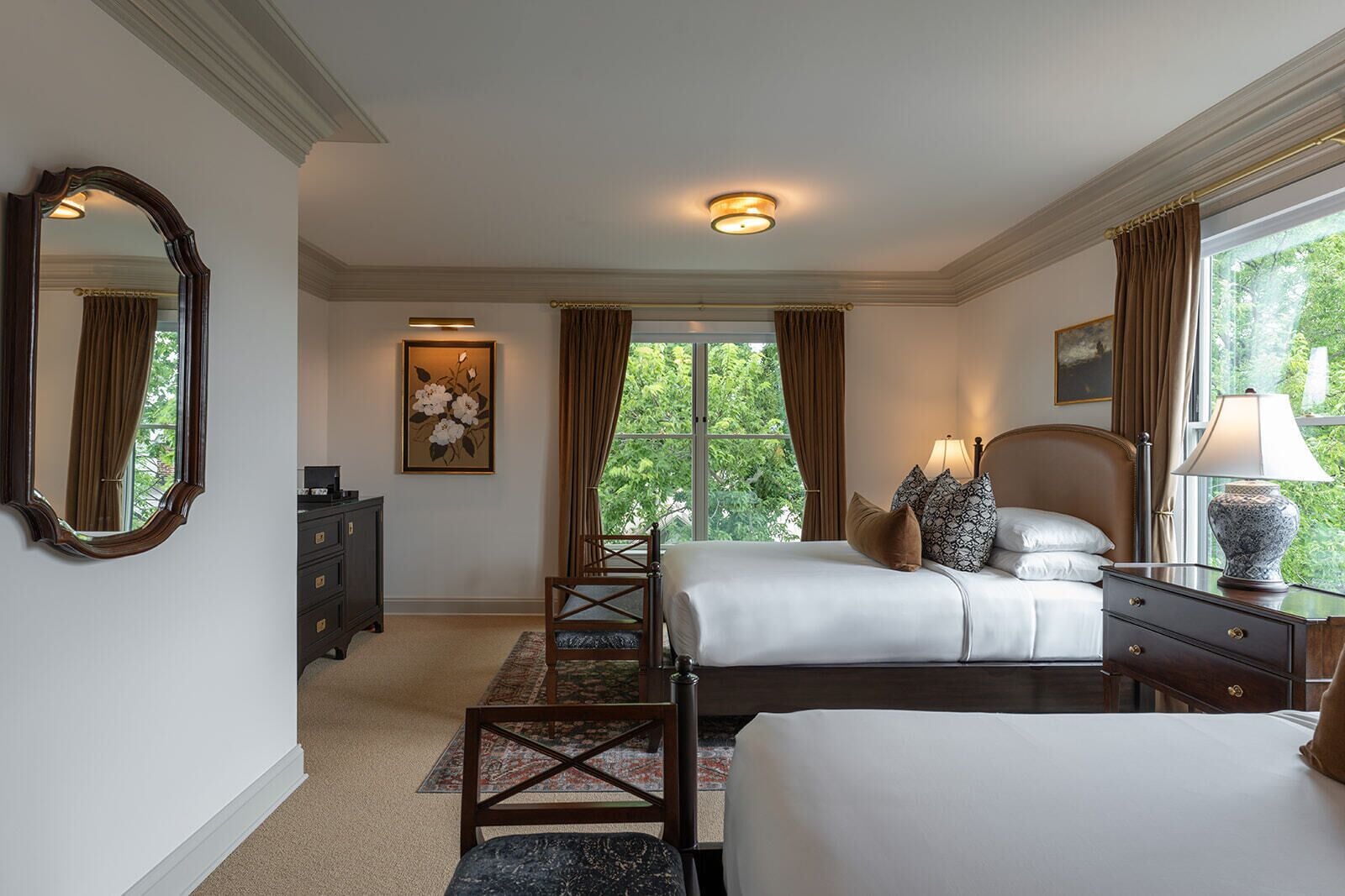 A hotel room with two beds, a dresser, a chair, a desk, and a large window with curtains.