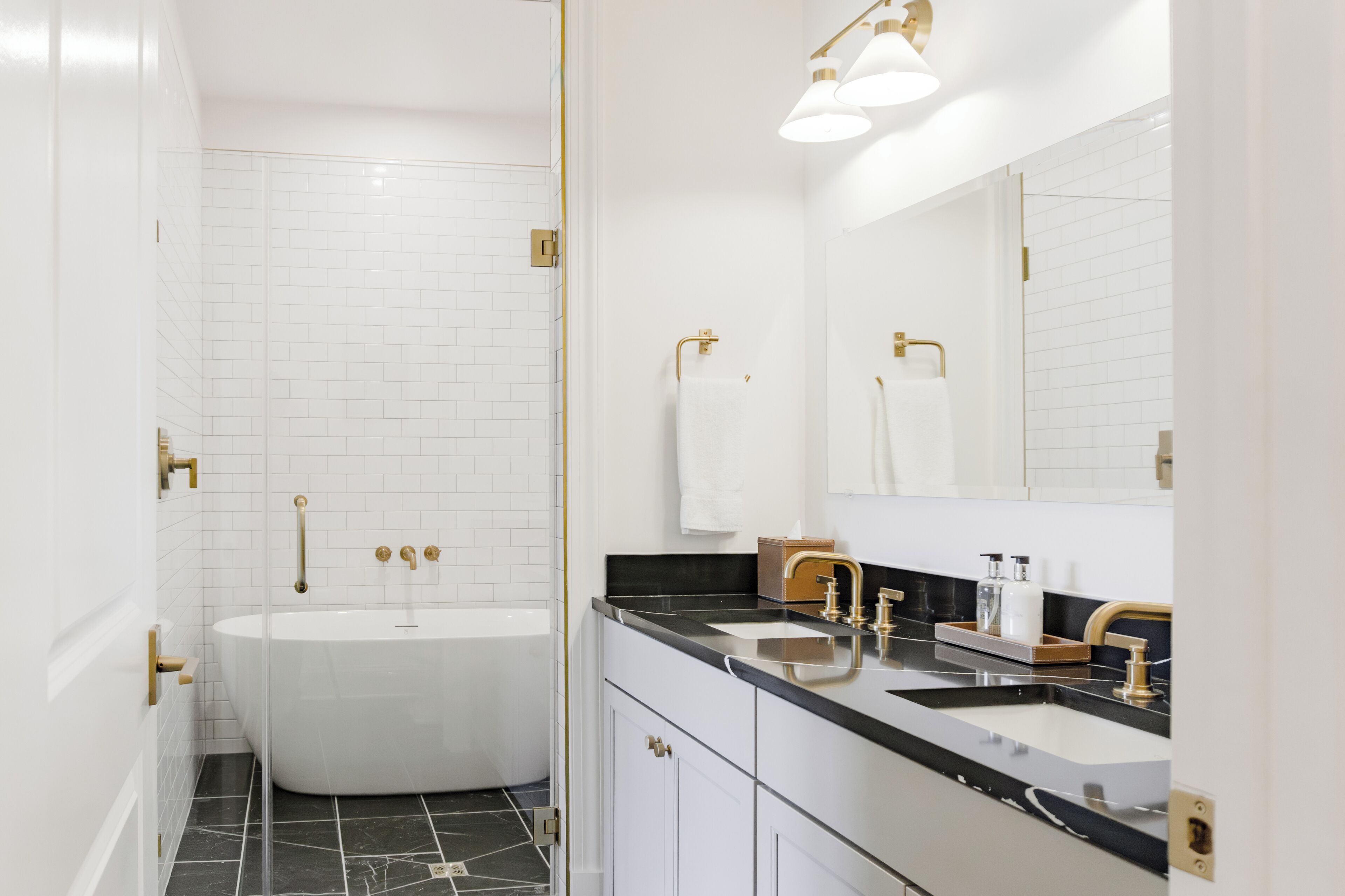 Une salle de bain moderne avec une baignoire sur pieds, un meuble-lavabo doté d’un plan de travail noir et un grand miroir.
