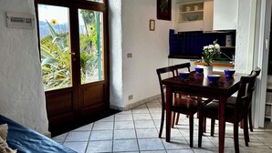 Een eethoek met een houten tafel en stoelen, uitzicht door een groot rondboogvenster, en een keuken met blauwe kastjes.