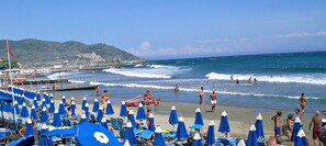 A beach with rows of blue umbrellas and beach chairs, a pier with boats, and people enjoying the water. - Panoramic Rural House With Garden (Chiusanico)