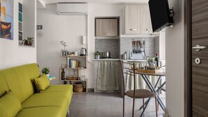 A compact living space with a sofa, a dining area with a table and chairs, a kitchen with cabinets and a TV mounted on the wall.