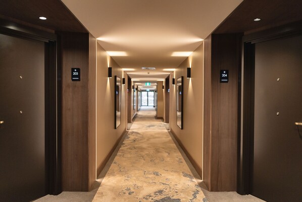 Een hotelgang met houten deuren, genummerde bordjes en een vloerbedekking.