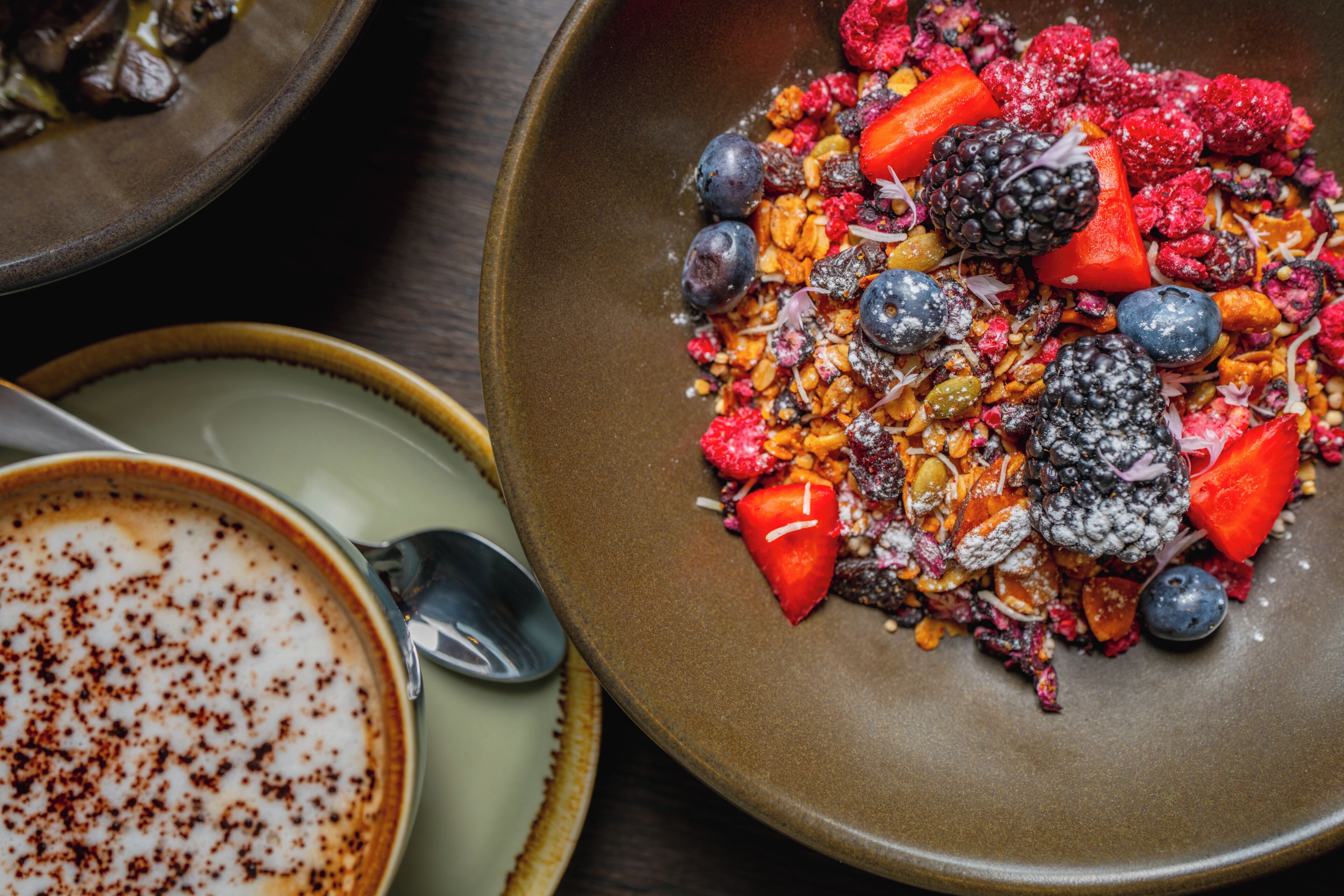Un bol de fruits rouges variés et de granola, présenté sur une assiette en céramique.