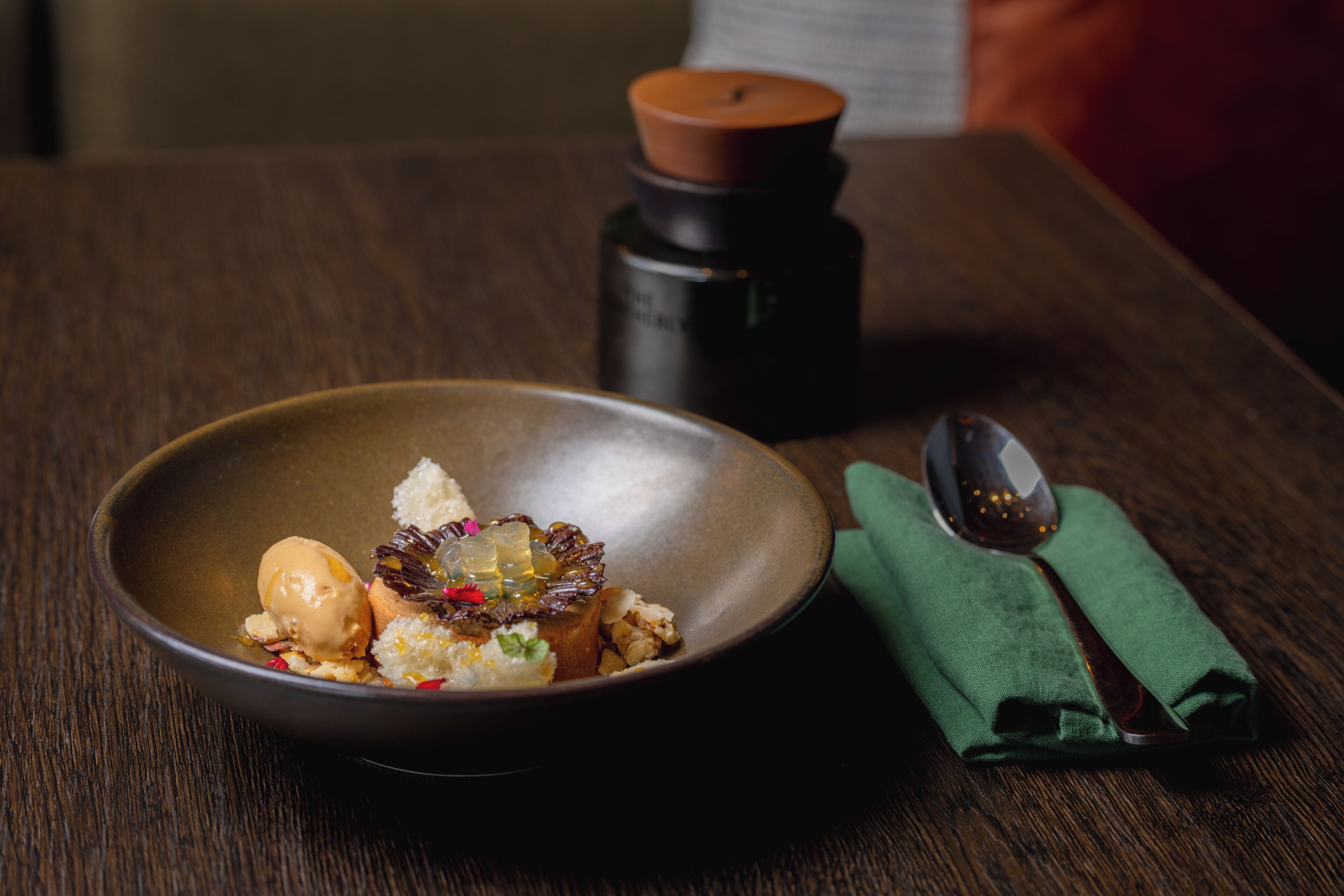 A bowl of food on a wooden table with a spoon and a green napkin.