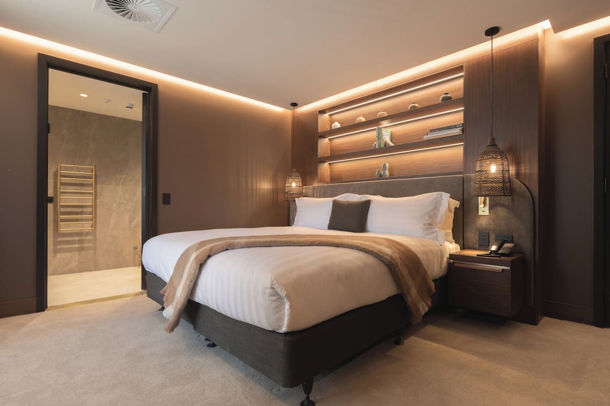 Une chambre à coucher moderne avec un grand lit, des étagères intégrées, une table de chevet avec une lampe et un dressing.