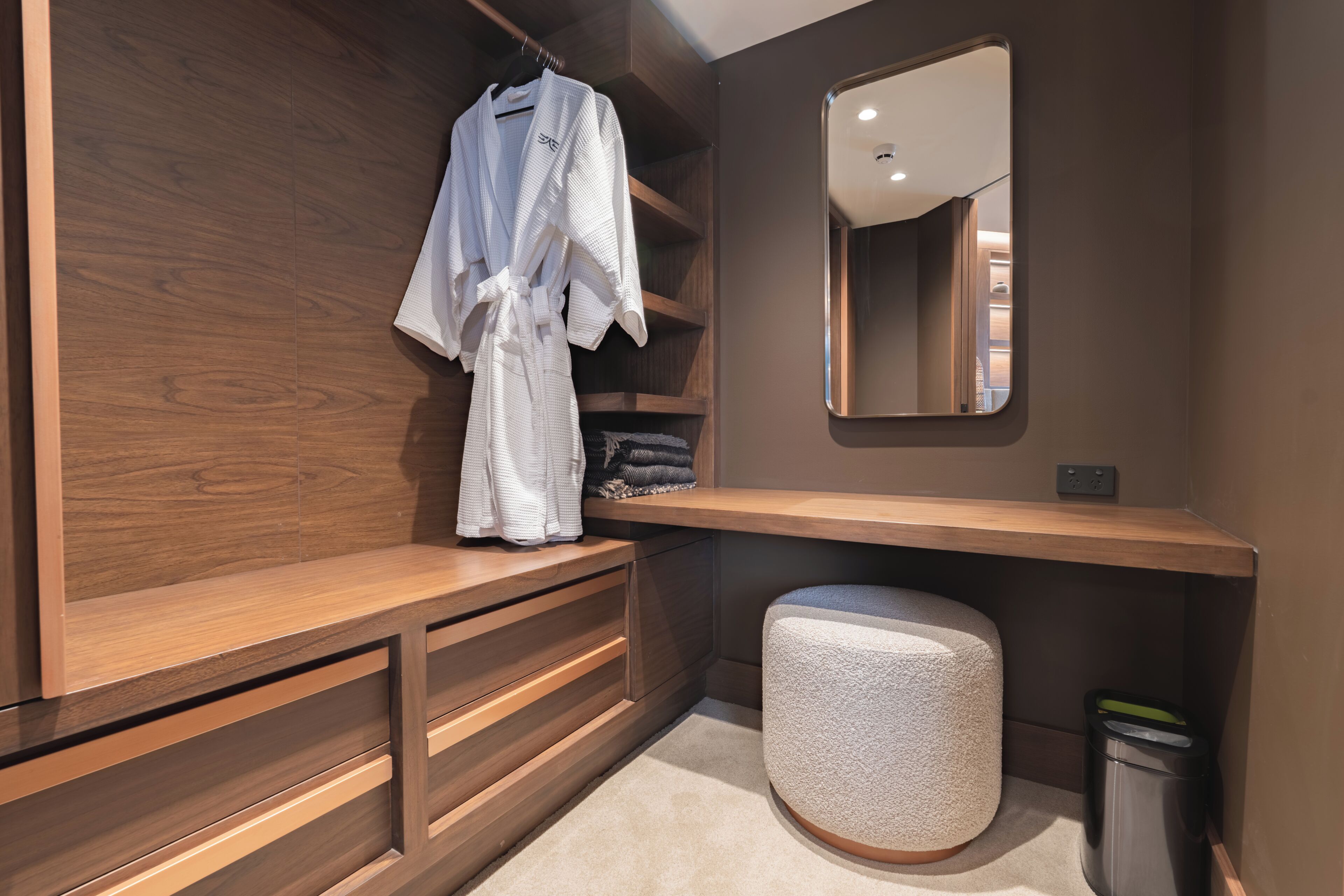 Un baño moderno con tocador de madera, un espejo y una bata colgada en un perchero.