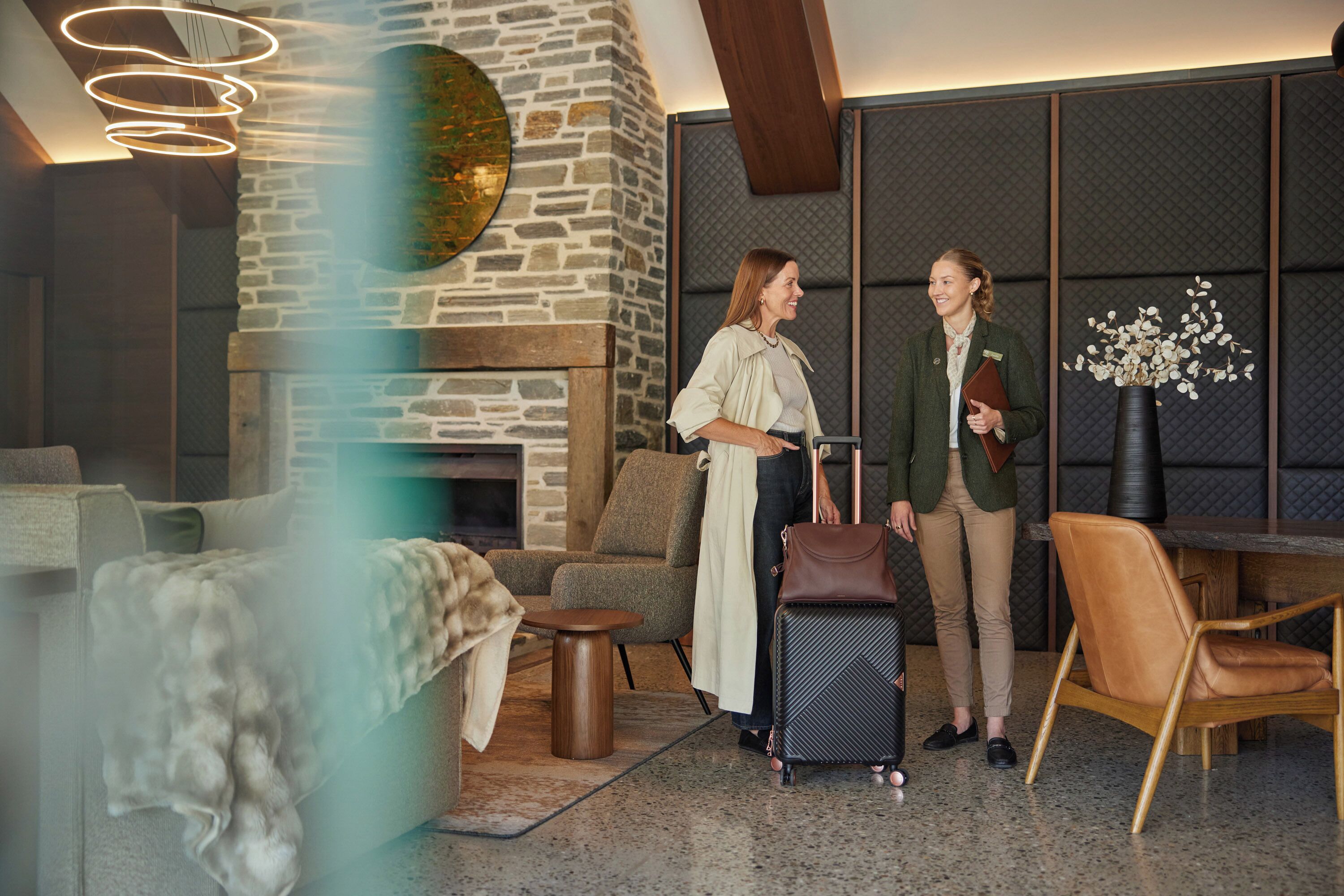 Un hall d’hôtel moderne avec une cheminée en pierre, des sièges confortables et un luminaire élégant.