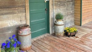 Un bâtiment rustique en bois, avec une porte verte et une enseigne indiquant « Magasin général », ainsi que deux plantes en pot sur le porche.