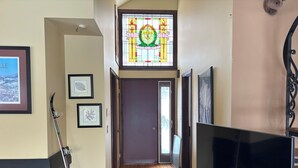 Un couloir doté d’un plancher en bois, d’un extincteur, de tableaux encadrés, d’un téléviseur et d’une fenêtre à vitraux.