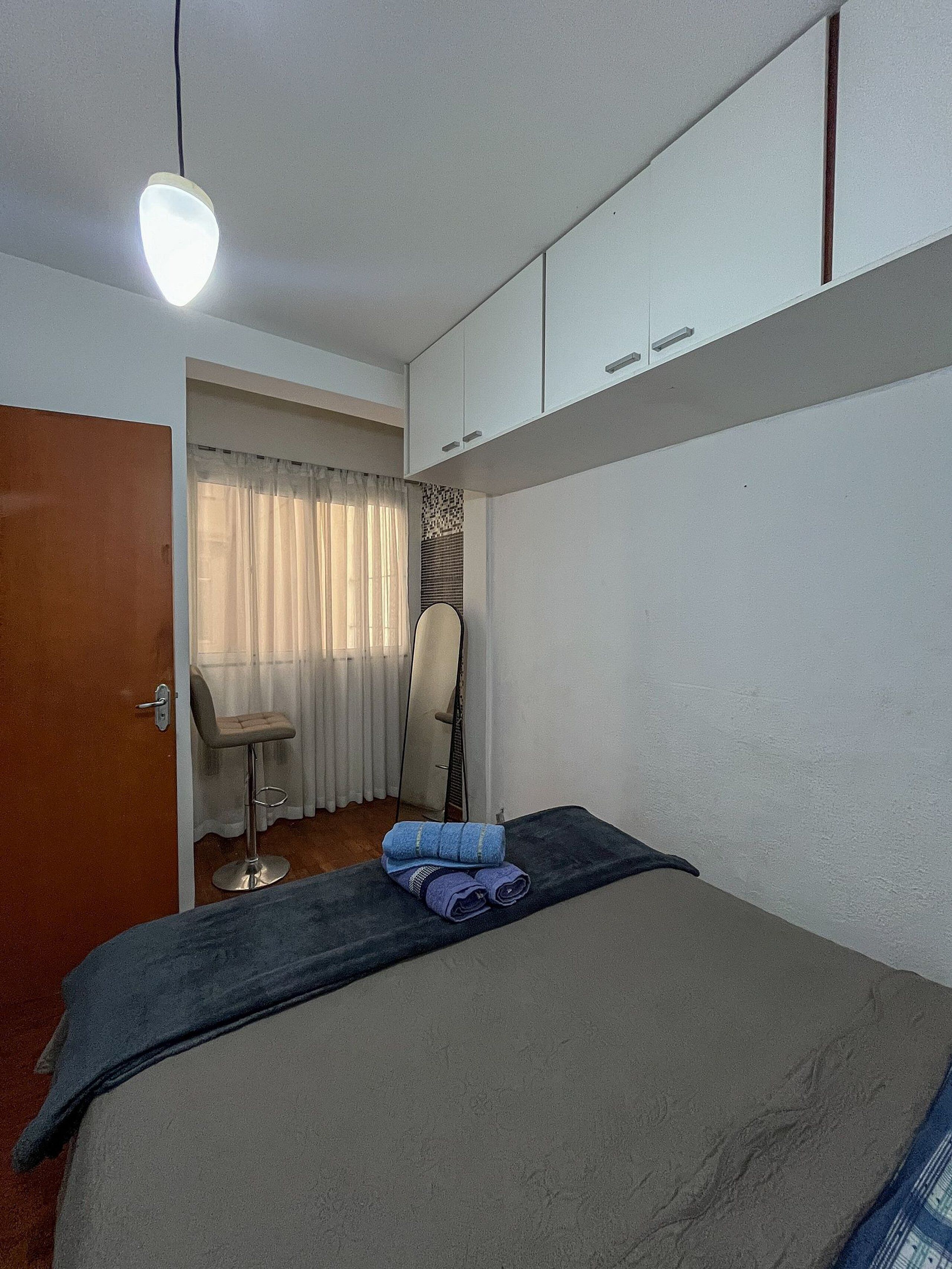 Un dormitorio con cama, una silla, un espejo y un armario.