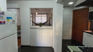 A compact kitchen with a refrigerator, a microwave, and a stove. There is a small countertop with a plant and a hanging light fixture. - Spacious apartment on Copacabana beach (Rio de Janeiro)