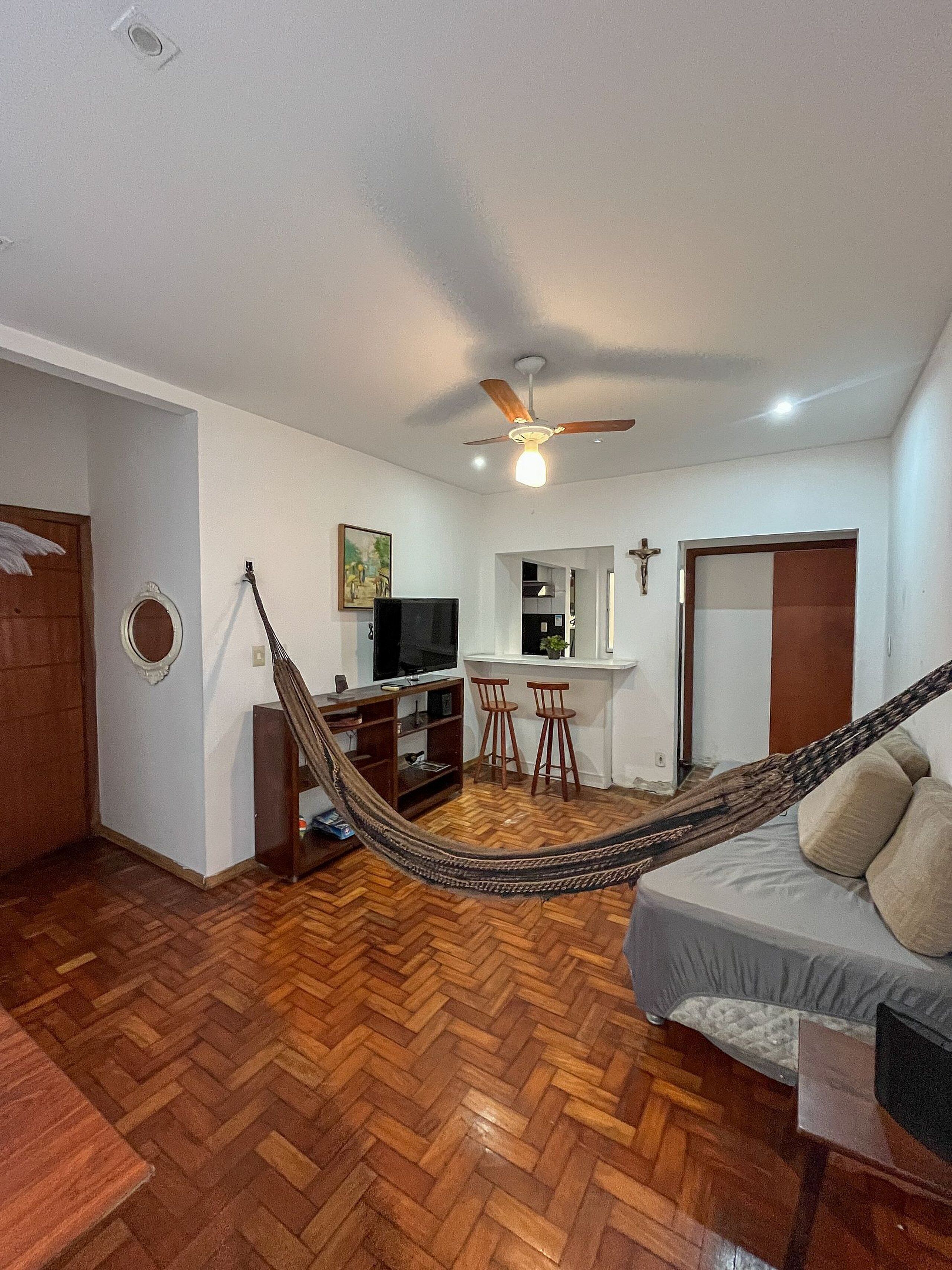 A room with a hammock, a bed, a television, a dining area, and a ceiling fan.