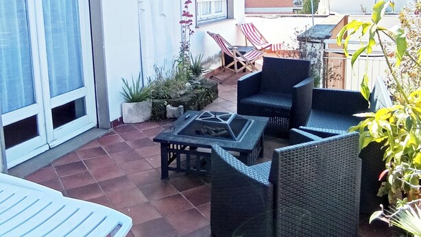 Une terrasse extérieure avec un espace salon comprenant une table et des chaises, le tout entouré de plantes en pot.