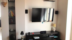 Un salon moderne avec un téléviseur à écran plat fixé au mur, un meuble noir pour appareils électroniques en dessous et un canapé vert.