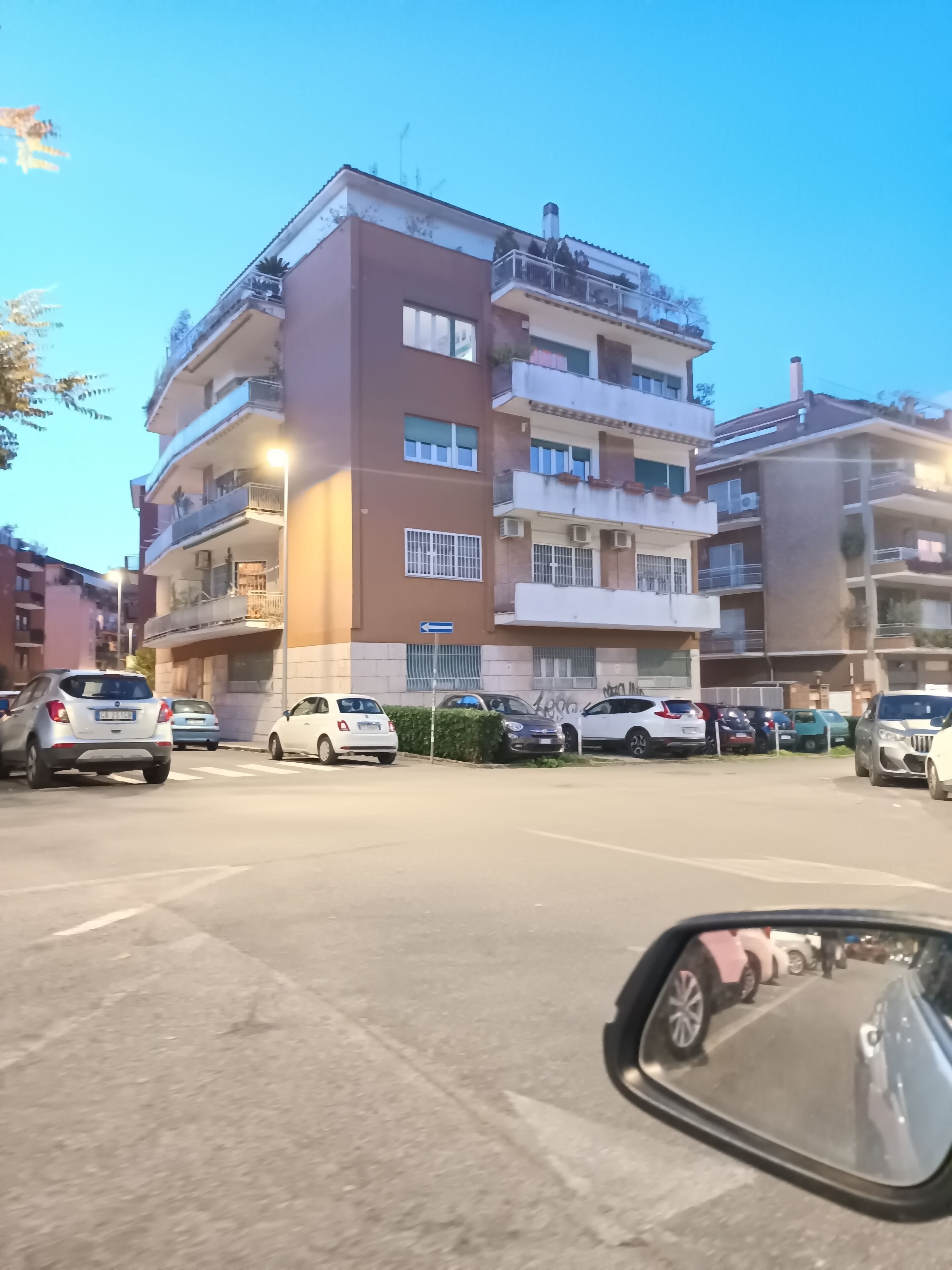 Un edificio residenziale a più piani con balconi, auto parcheggiate e cielo sereno.