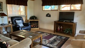 Ein gemütliches Wohnzimmer mit Kamin, Ledersessel, Couchtisch aus Holz und einem Fernseher auf einem Holzboden.