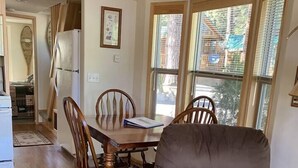 A dining area with a wooden table and chairs, a grey armchair, and large windows with blinds. - Cabin #23 at Hyatt Lake Resort (Jackson County)