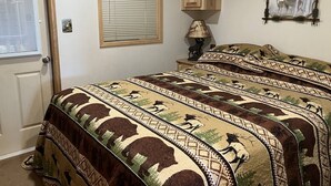 Een slaapkamer met een bed met beddengoed met een patroon, een raam met zonwering, houten kasten en een wandlamp.