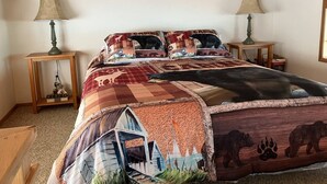 Een slaapkamer met een houten plafond, twee nachtkastjes, een bed met een quilt met dierenprint en een lamp op elk nachtkastje.