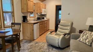 Un espacio habitable compacto con zona de cocina, una mesa de comedor con sillas, un sillón reclinable y un sofá.