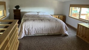 Een slaapkamer met een groot bed, een houten hoofdbord, een klein houten kastje en een raam met blinds.