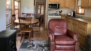 Een kleine keuken met houten kastjes, een eettafel met stoelen, een rode leren fauteuil en een fornuis.