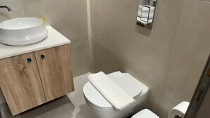 A modern bathroom with a white sink, wooden cabinet, toilet, and a toilet paper holder. - Petite Fleur Apartment (Lefkada)