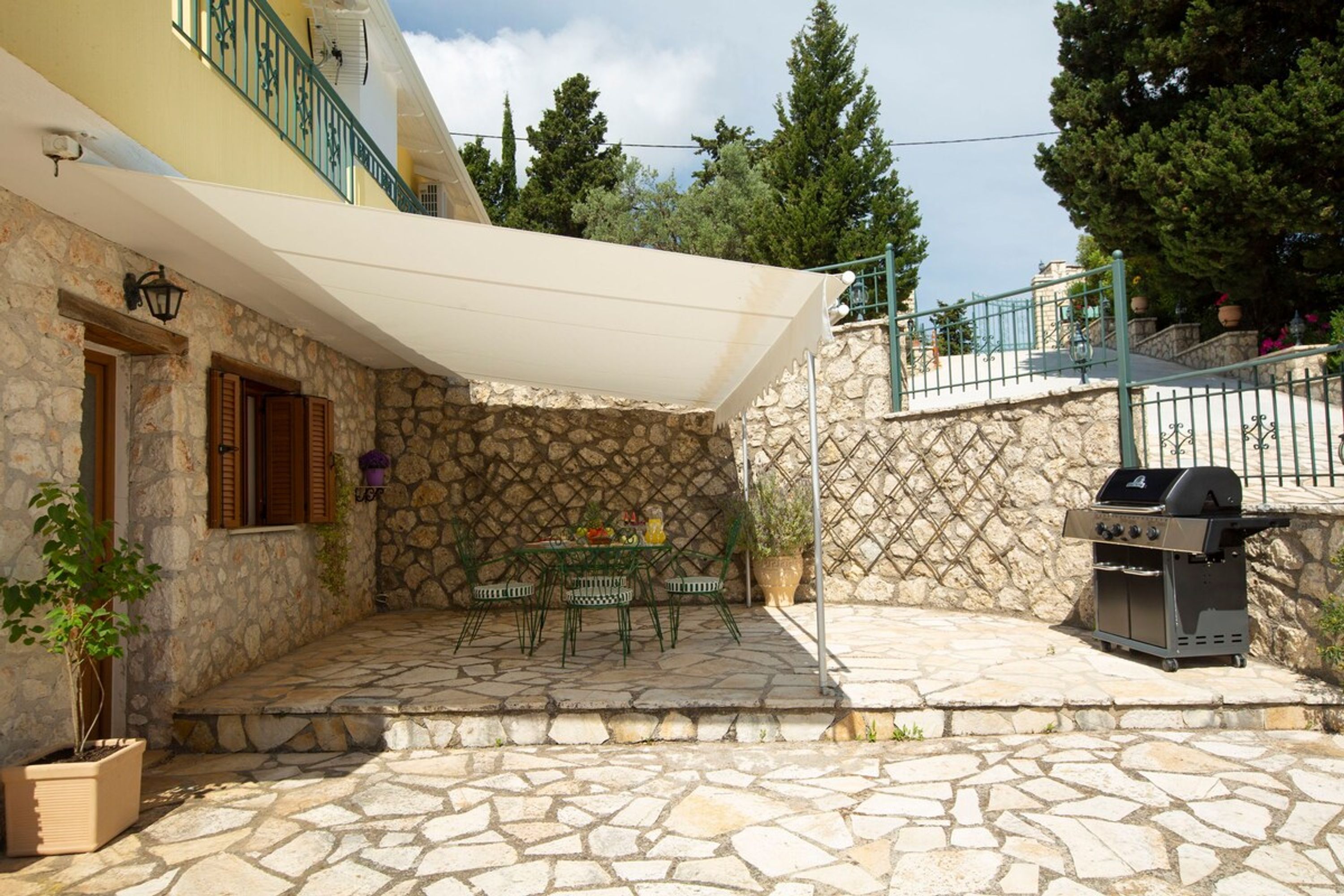 A stone patio with a table and chairs, a grill, and a covered area with a railing.