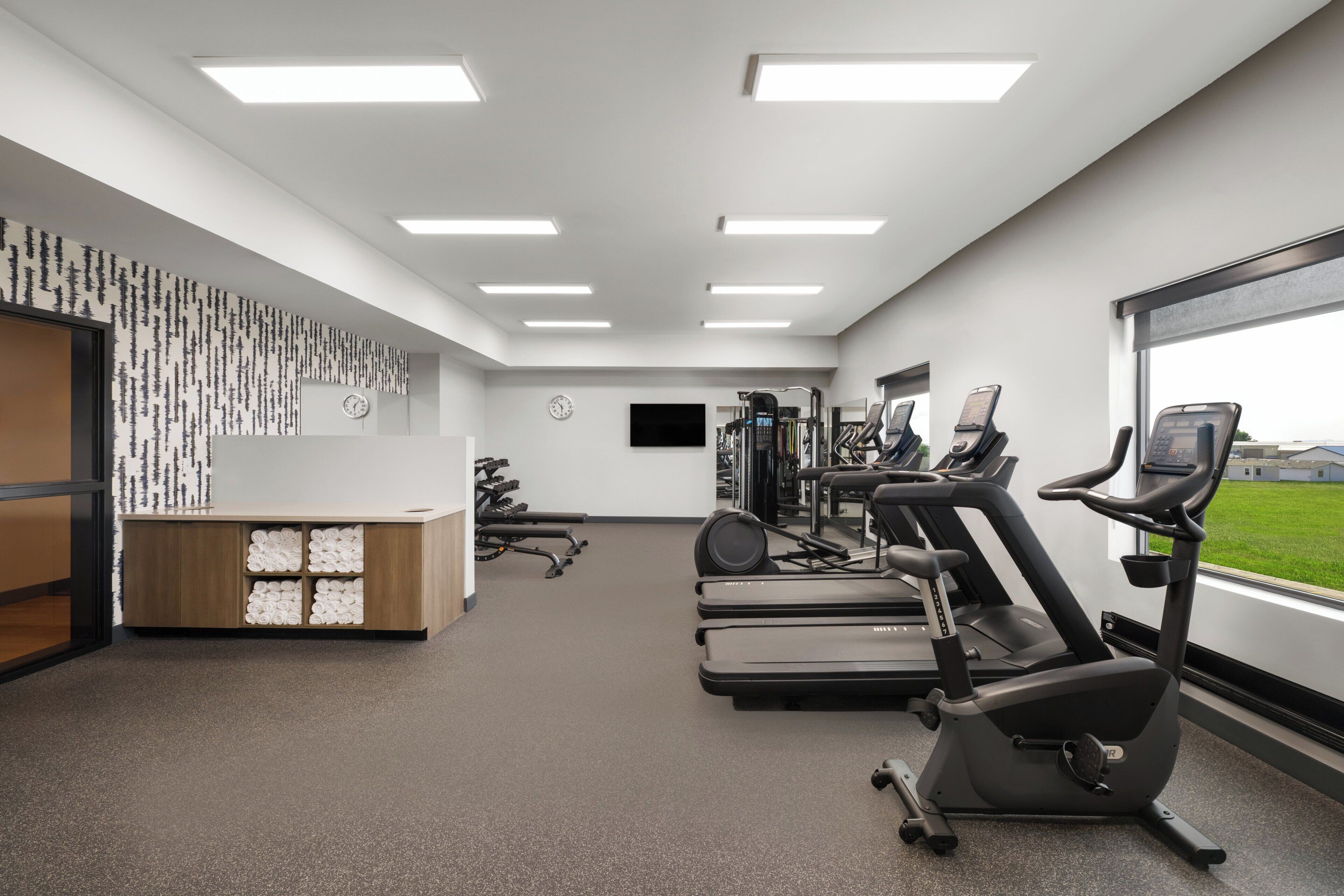 A gym with exercise equipment, a reception desk, and a large window with a view.
