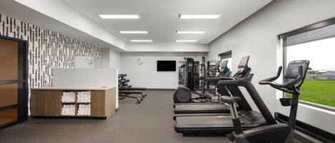 A gym with exercise equipment, a reception desk, and a large window with a view.